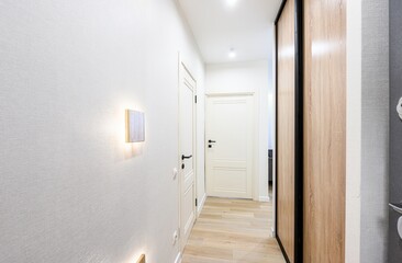 bright hallway with white walls, wooden floors, and interior doors. Features include a wooden wall lamp and a sliding door wardrobe
