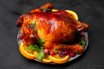 Whole Christmas baked chicken with cranberries and oranges on black background