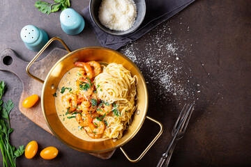 Pasta with shrimps in creamy sauce in a pan on dark background top view