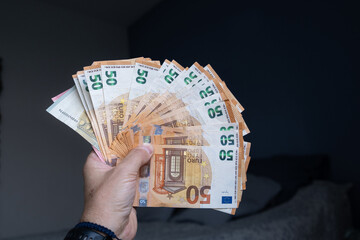 Hand holding fanned-out modified euro bills indoors. Concept of personal wealth, cash savings, economic power or success. Money props for commercial and financial use.