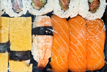 Sushi set in a plastic takeaway box with salmon nigiri, shrimp ebi, tamago and maki rolls, rice and...