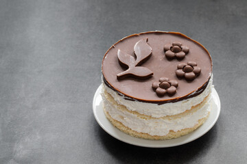 Small Cake with Vanilla souffle, biscuit, with chocolate, chocolate decor on top. On a plate. Dark background. Copy space