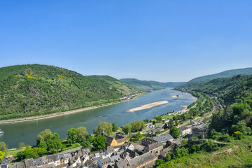 Rhine Valley near Bacharach, Germany: A panoramic view of the river winding through the steep valley, with forested hills and terraced vineyards overlooking a small town on the bank.

