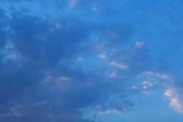 Obraz premium Scenic view of the sky with deep blue tones and scattered clouds illuminated by warm sunlight, capturing a calm and serene early evening atmosphere.