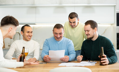 Fototapeta premium Happy friends drinking beer after solving their financial problems while sitting together at a home cooking table