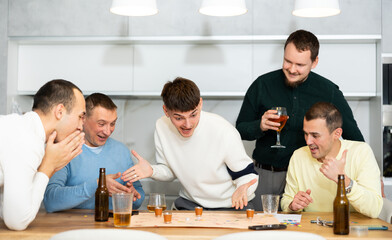 Friends drinking beer and enthusiastically playing a board game at home