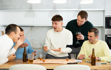 Group of adult friends excitedly playing board games and drinking beer at home
