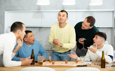 Lively group of men spending free time together during bachelor gatherings, engaged in drinking board game, where losing turn meaning taking shot, in warm friendly home environment..