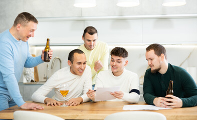 Male friends read a financial or legal document, drink beer and try to solve financial problems by...