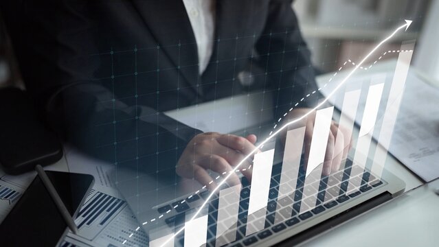 A business professional analyzes financial data on a laptop, featuring a growth chart overlay that visualizes market trends and insights in a dynamic office setting. Copula - Powered by Adobe