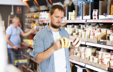 Man buys sticky adhesive tape in construction store for carrying out internal and external finishing work on object. Repair items, paint and varnish products, accessories, supermarket