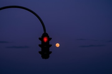 Red traffic light at night with full moon in deep twilight sky
