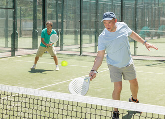 Adult men in doubles playing paddle tennis on tennis court