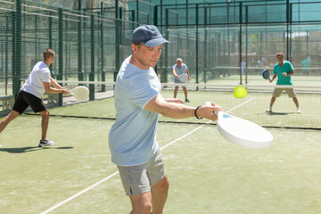 Men play padel on an outdoor tennis court. Hitting the ball with a racket
