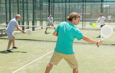 Men play padel on an outdoor tennis court. Hitting the ball with a racket