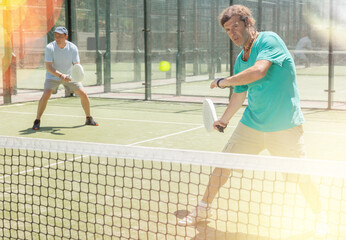 Men play padel on an outdoor tennis court. Hitting the ball with a racket