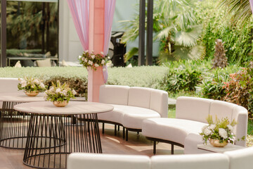 Elegant event setup with white seating and floral centerpieces. Perfect for outdoor gatherings and celebrations. Serene garden atmosphere.