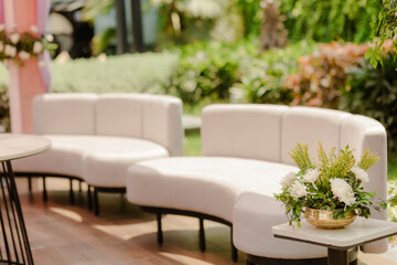 Outdoor event seating area featuring curved white sofas and floral arrangements, creating a relaxed and stylish setting for guests to socialize.