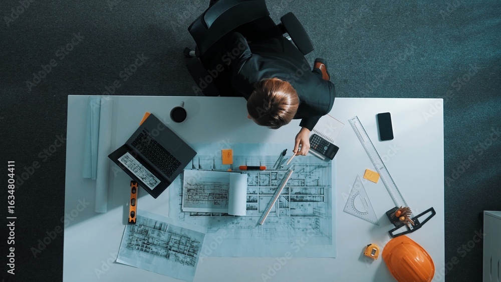 Poster top view of skilled manager looking at blueprint and talking to engineer sitting at meeting table wi