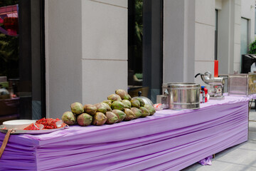 Outdoor food preparation: Fresh coconuts and a shaved ice machine on a purple draped table....