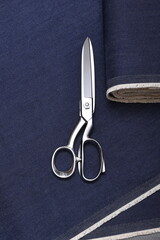 Professional sewing scissors rest atop a bolt of deep blue denim fabric, representing...