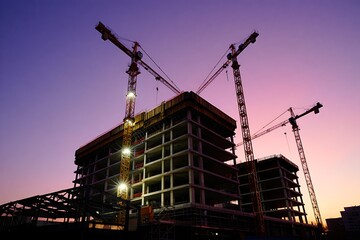 Construction site with cranes and unfinished building at sunset