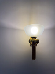 Minimalist wall lamp emitting warm light, creating soft shadows on a neutral wall background.