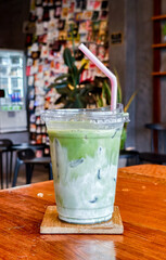 Refreshing Matcha Latte: A close-up shot of a vibrant green matcha latte, ice-cold and refreshing, in a clear plastic cup with a pink straw, sits invitingly on a wooden table.