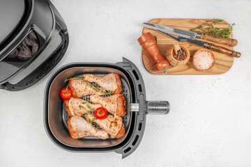 Raw marinated chicken drumsticks with herbs and tomatoes in an air fryer basket ready for cooking. top view. copy space