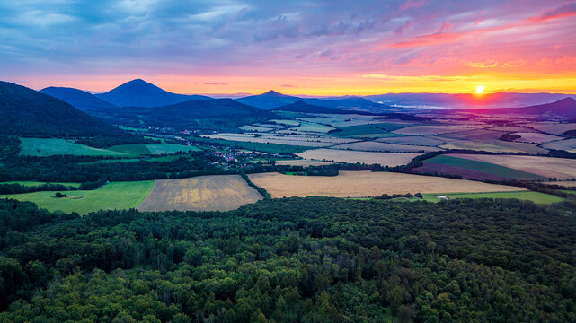 Colorful sunrise over rural landscape of Czech Central Highlands, showing fields, hills and forests from aerial drone view, capturing peaceful countryside and vibrant morning sky