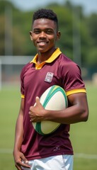 Confident young man holding a rugby ball in a sunny field
