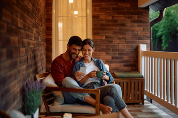 Happy couple enjoying while using smart phone on porch.