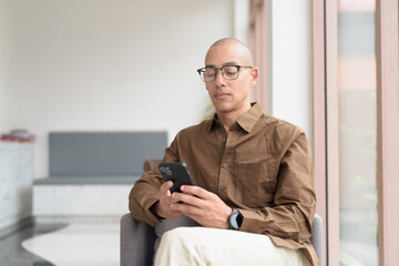 Confident bald Latin man using smartphone in coffee shop, casual tech-savvy lifestyle with glasses