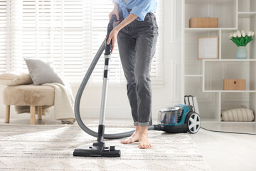 Woman cleaning carpet with vacuum cleaner at home, closeup