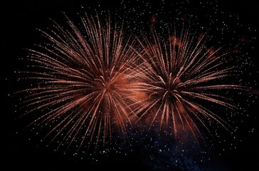 Two vibrant, copper-toned fireworks bursts illuminate the night sky, their radiant trails extending outwards against a backdrop of scattered stars