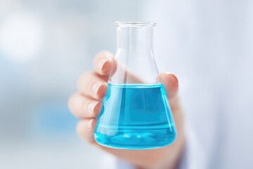 Hand holding laboratory flask filled with vibrant blue liquid, s