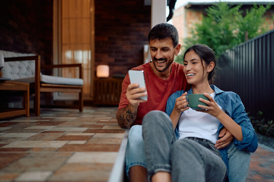 Happy couple using smart phone while enjoying in afternoon on their porch.