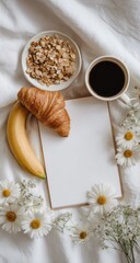 Flatlay of breakfast coffee, croissant, banana, granola, blank notepad, and daisies on white bedding