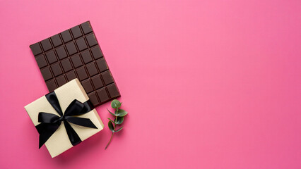 Dark chocolate bar and gift box with black ribbon on pink background