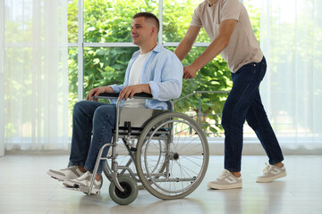 Caregiver with man in wheelchair near window indoors, closeup