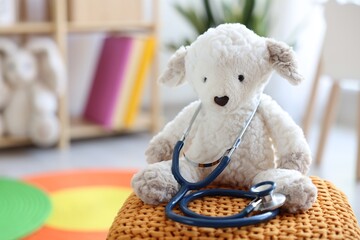 Pediatrician concept. Toy sheep and stethoscope on pouf in clinic, closeup. Space for text