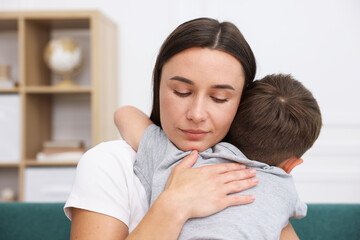 Mother supporting and hugging her sad son on sofa at home