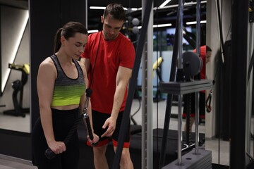 Young woman exercising with lat pulldown machine with professional personal trainer in gym