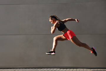 Woman in sportswear running near building outdoors, space for text