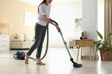 Woman cleaning floor with vacuum cleaner at home, closeup