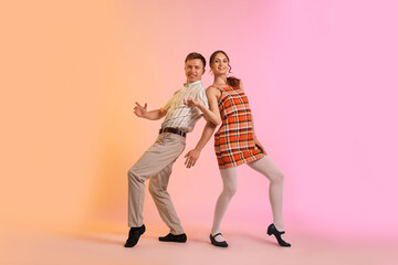 Happy couple in retro outfits dancing on color background