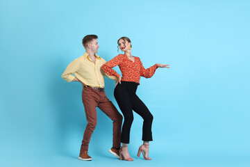Happy couple in retro outfits dancing on light blue background