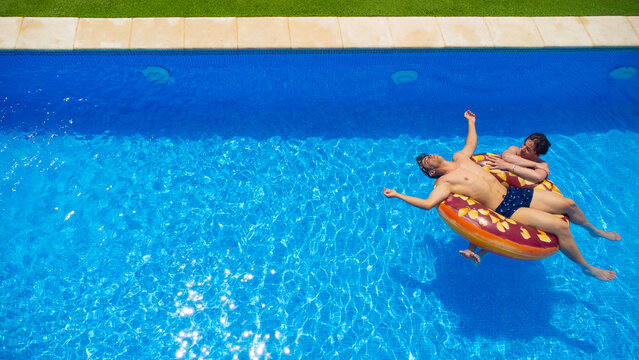 Young couple relaxing on a pastry ring pool float in clear blue water on a sunny day, the girl watches as the boy rests with his arms open with his head partially in the water - Powered by Adobe