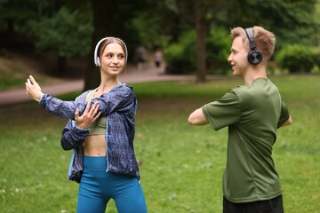 Happy couple in headphones doing morning exercises in park