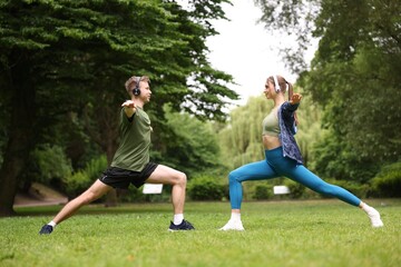 Happy couple in headphones doing morning exercises in park